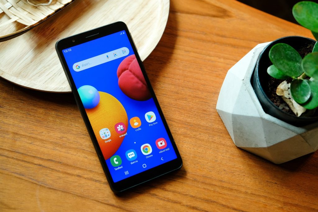 Foto do Samsung Galaxy Samsung Galaxy A01 Core em cima de uma mesa de madeira. Ele está apoiado em um prato, com a tela virada para cima. No canto direito da tela, aparece um pequeno vaso de planta.