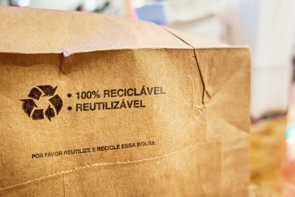 Sacola de papel com símbolo de reciclagem e com escritos: 100% reciclável e reutilizável.