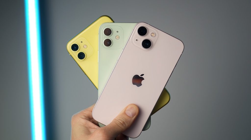 iPhone 11 amarelo, iPhone 12 verde e iPhone 13 rosé segurados por uma pessoa.