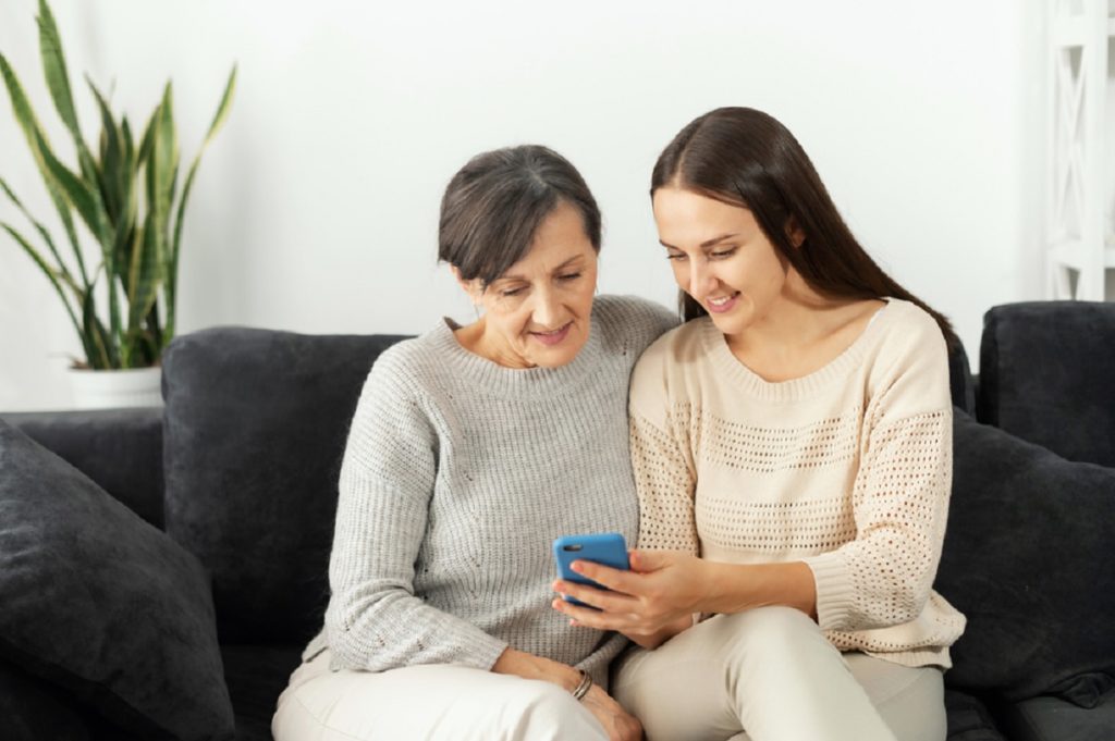 Uma filha adulta ajuda a mãe a descobrir como usar um smartphone, duas mulheres multigeracionais sentadas no sofá e olhando para a tela do telefone