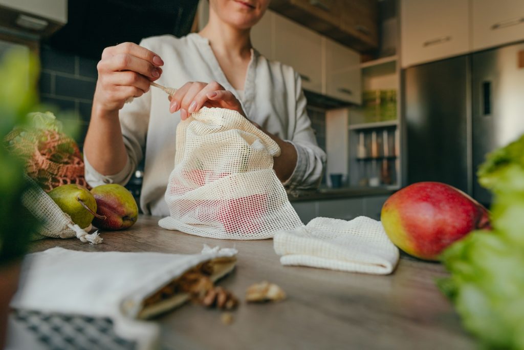 Jovem mulher segurando o saco de produtos reutilizáveis ​​de algodão orgânico com pimentas em cima da mesa na cozinha. Zero desperdício e conceito de embalagem sustentável.