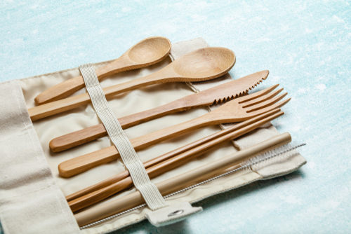 Colheres, facas e garfos de bambu dispostos em uma bolsinha de pano aberta.