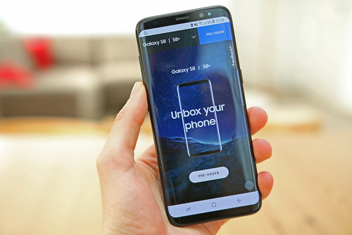 Mão segurando o um Samsung Galaxy S8 com a tela em primeiro plano.