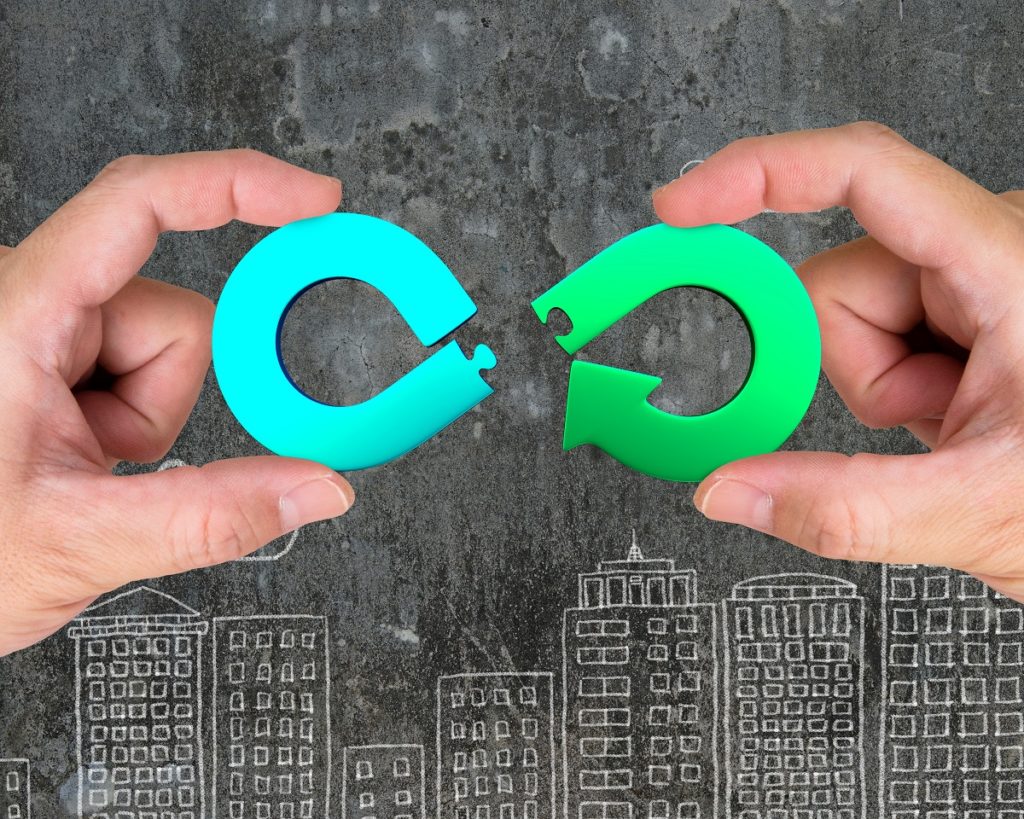 Conceito de economia circular. Duas mãos montando seta infinito símbolo de reciclagem de quebra-cabeça peças, em edifícios da cidade doodles fundo.
