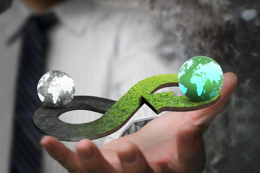 Conceito de economia circular verde. Mão mostrando símbolo infinito seta com textura de grama e dois globos de cores diferentes.