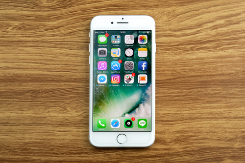 Foto de um iPhone 7 branco sobre uma bancada de madeira. A tela está ligada e virada para cima.