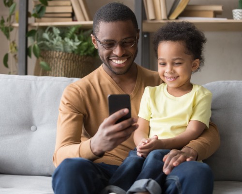 Pai e filho sentados no sofá olhando para a tela do smartphone. 