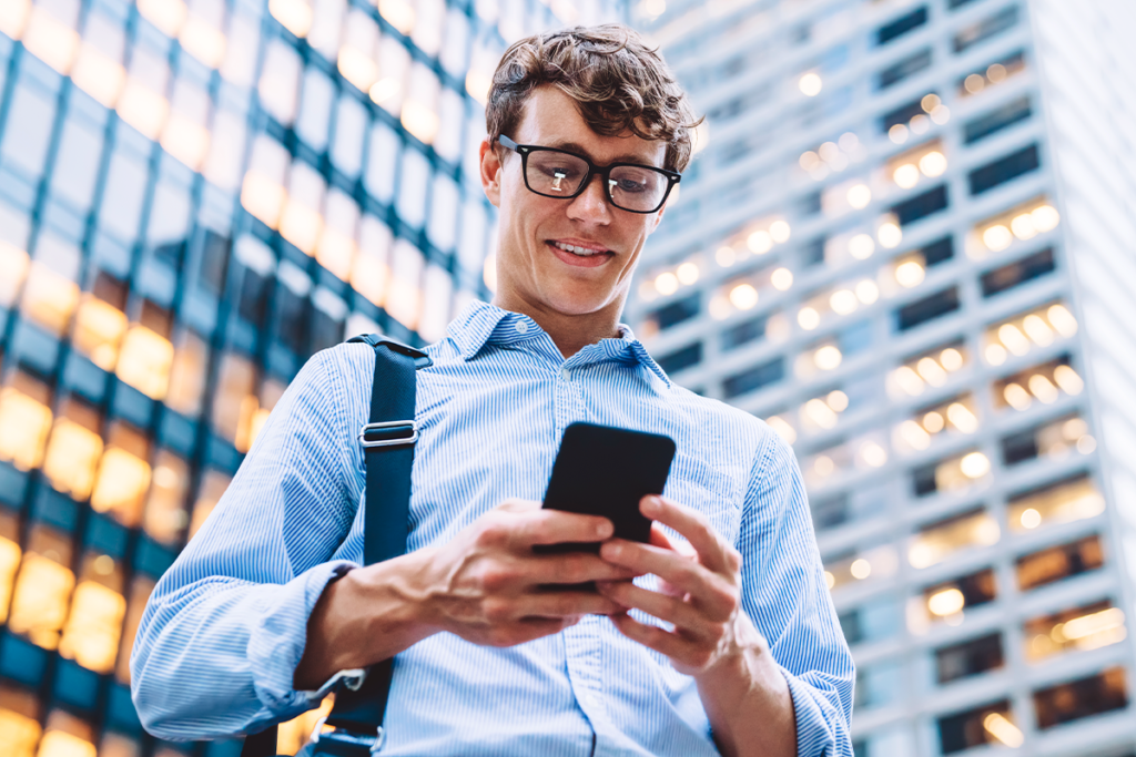Homem de óculos pretos e camisa social azul com celular nas mãos.