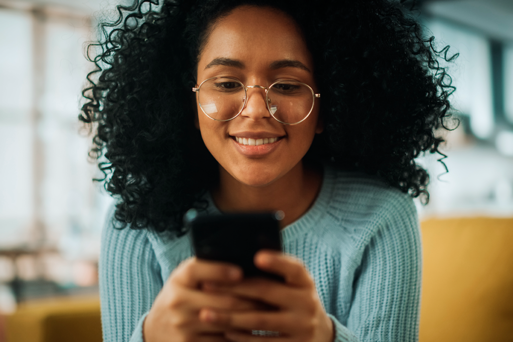 mulher negra com blusa comprida azul , segurando celular com as duas mãos.