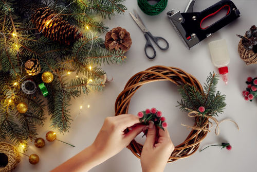 As mãos femininas decoram a guirlanda de Natal com ramos de abeto com uma baga vermelha e cones da floresta. Fundo branco. Conceito de ano novo.