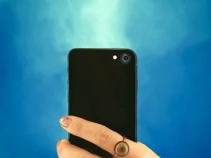 Fundo azul celeste com mão feminina segurando um smartphone preto com a traseira virada para frente. 