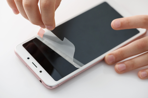 Mãos removendo a película de proteção da tela do smartphone.