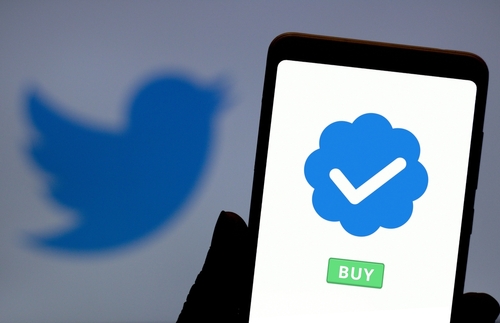 Tela do celular com selo azul de verificação e um botão verde com escrito "buy". No fundo, aparece a logo do Twitter. 