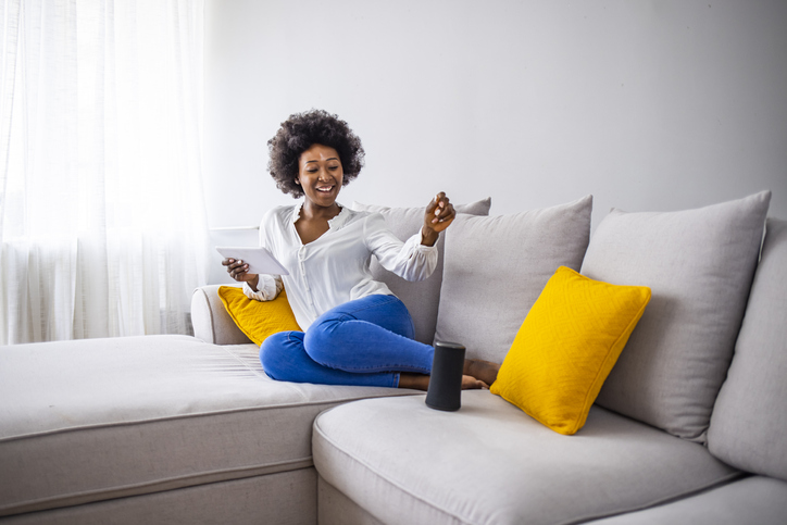 Coluna sem fio inteligente com uma jovem controlando dispositivos domésticos com comandos de voz em segundo plano em casa. Mulher controlando dispositivos domésticos com comandos de voz