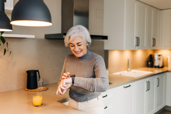 Mulher sênior sorrindo para seu smartwatch em pé na cozinha. Mulher idosa feliz monitorando sua frequência cardíaca e condicionamento físico em um aplicativo móvel.