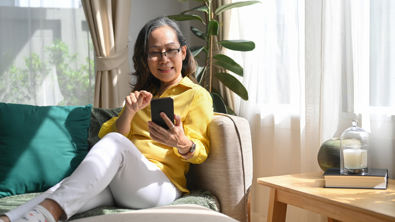 Mulher madura sorridente conversando com parentes online, fazendo compras, verificando as mídias sociais no telefone inteligente.