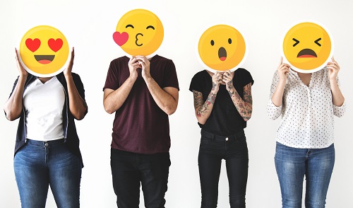 Pessoas diversas segurando placas de emojis na altura do rosto. 