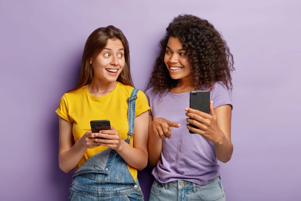 Duas jovens discutindo qual celular comprar, comparando opções de smartphones com sorriso e entusiasmo, ideal para conteúdo sobre compare celular