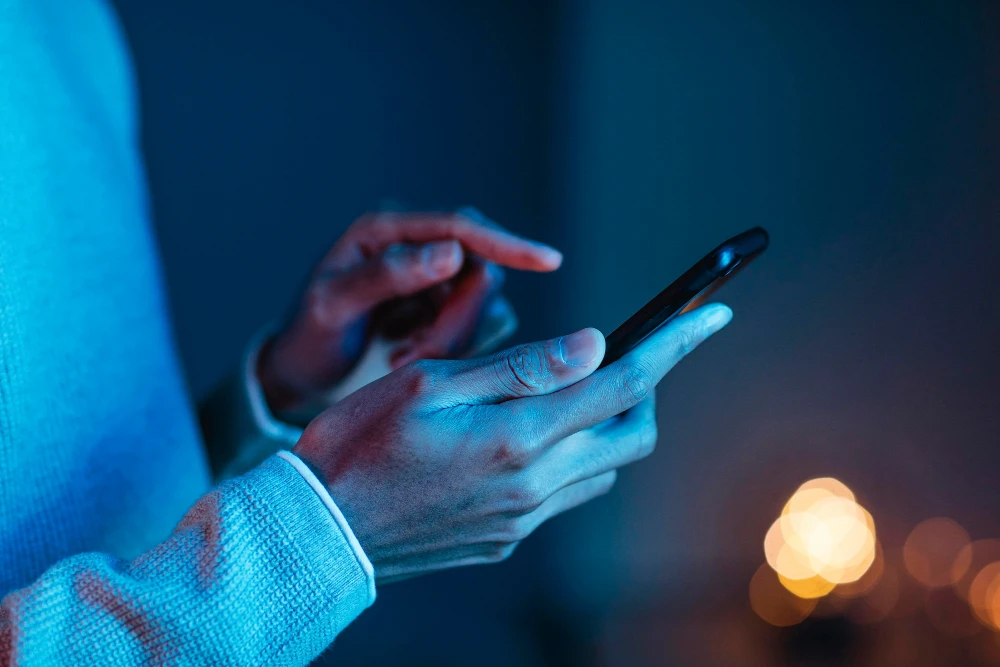 Pessoa usando smartphone com o sistema One UI 8.0 em ambiente com iluminação baixa, destacando a interface moderna e funcional.